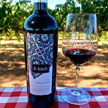 Bottle of Graciano wine from Lodi Winegrape Commission with a glass of red wine on a vineyard table.