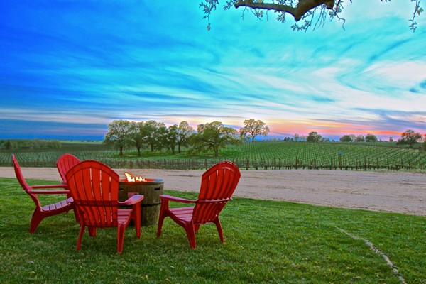 Red Adirondack chairs and fire pit overlooking a vineyard at sunset in Lodi, California.