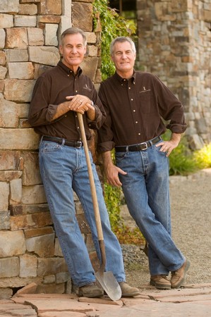 Two men in casual attire standing outdoors by a stone wall, representing Lodi Winegrape Commission.