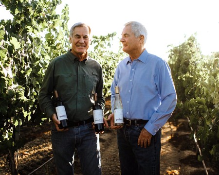 Two men in vineyard holding wine bottles, discussing wine quality and grape growing in Lodi, California.