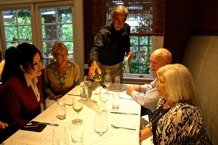 Group of people enjoying wine tasting at a restaurant with a server pouring wine.