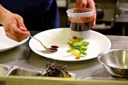 Chef drizzling sauce on a gourmet dish with fresh greens and vegetables, showcasing Lodi wine and local produce.