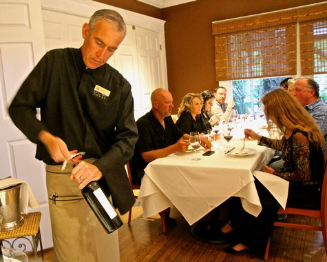 Guests enjoying a wine tasting dinner at a Lodi Winegrape Commission event with a server pouring wine.
