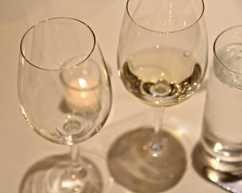 Two wine glasses and a water glass on a table, with reflections and shadows, representing wine tasting.