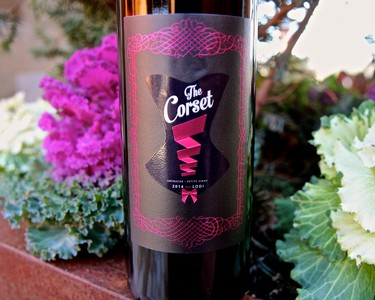 Close-up of a wine bottle labeled 'The Corset' with vibrant flowers in the background.