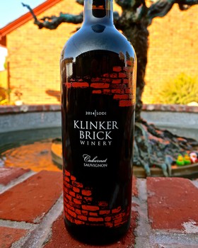Bottle of Klinker Brick Winery Cabernet Sauvignon with brick wall background and outdoor setting.