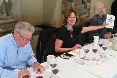 Woman presenting wine tasting results at Lodi Winegrape Commission event with seated attendees and wine glasses.