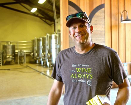 Smiling man at Lodi wine event with wine tanks in background.