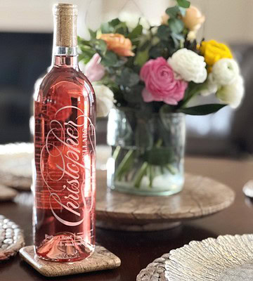 Elegant rosé wine bottle from Lodi Winegrape Commission with a floral arrangement in the background.