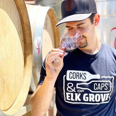 Man tasting red wine at Lodi Winegrape Commission with wine barrels in background.