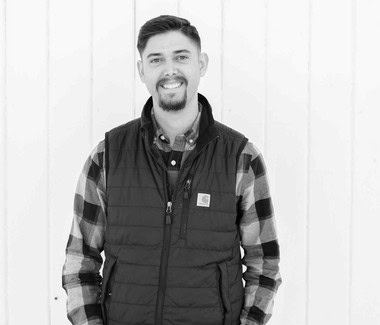 Smiling man in outdoor setting wearing a black vest and plaid shirt, Lodi Winegrape Commission.