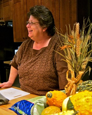 Smiling woman at Lodi Winegrape Commission event with wine and harvest decorations.