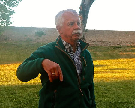 Elderly man in green jacket pointing at vineyard during sunset in Lodi, California.