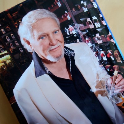 Senior man at wine tasting event with wine bottles in background.