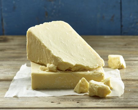 A large block of Parmigiano-Reggiano cheese with smaller chunks on a rustic wooden surface.