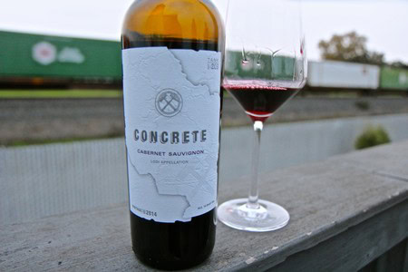 Bottle of Concrete Cabernet Sauvignon wine with glass of red wine on outdoor deck.