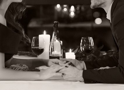 Couple holding hands across a table with wine glasses, candles, and a wine bottle in a romantic setting.