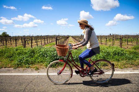 Woman riding a bicycle through a Lodi vineyard on a sunny day with blue skies and scattered clouds.