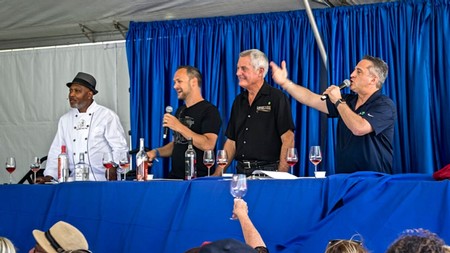 Panel of four men speaking at Lodi Winegrape Commission event with blue backdrop and wine glasses.