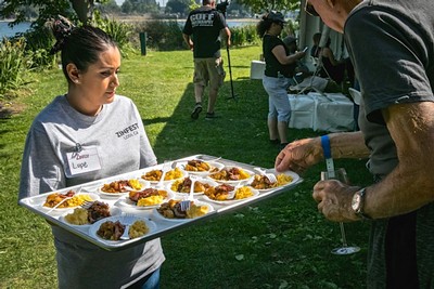 Woman serving wine and food at outdoor event organized by Lodi Winegrape Commission.