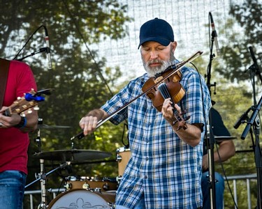 Man playing violin at Lodi Winegrape Commission outdoor event with musicians and trees in background.