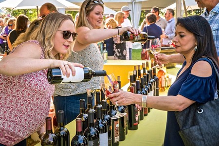 People enjoying wine tasting at an outdoor event with wine bottles on display.