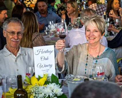 Smiling woman raising a glass of red wine at a wine tasting event with others in the background.