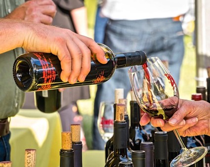 Person pouring red wine into a glass at a wine tasting event, with wine bottles on the table.