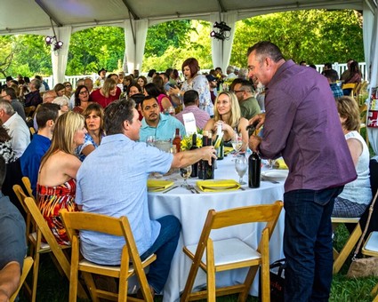 Guests enjoying a wine tasting event at an outdoor Lodi Winegrape Commission gathering under a large tent.