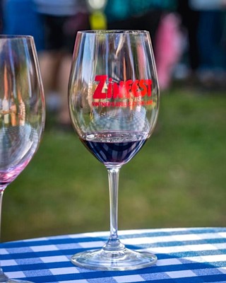 Wine glass with red wine at Lodi Winegrape Commission event, outdoor setting, vibrant atmosphere.