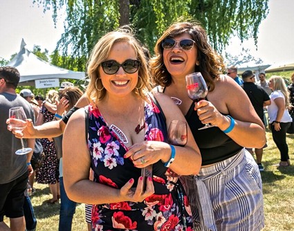 Two women enjoying wine at the Lodi Winegrape Commission outdoor event with a crowd in the background.