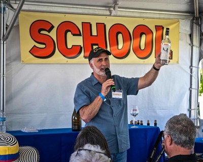 Man speaking at a wine event with a banner reading 'SCHOOL' in the background.