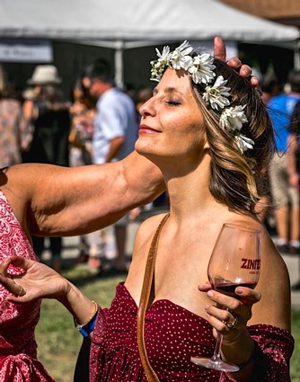Woman enjoying wine at Lodi Winegrape Festival with floral crown and wine glass in hand.
