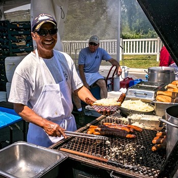 Smiling woman grilling sausages and hot dogs at Lodi Winegrape Commission event outdoors.