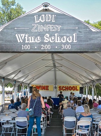 People attending Lodi ZinFest Wine School under a large tent with a speaker and audience.