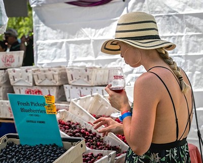 Woman tasting wine at Lodi Winegrape Commission booth with fresh berries display.