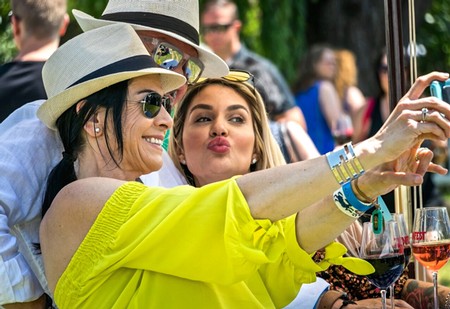 Two women enjoying wine at a Lodi Winegrape Commission outdoor event, taking a selfie with wine glasses in hand.