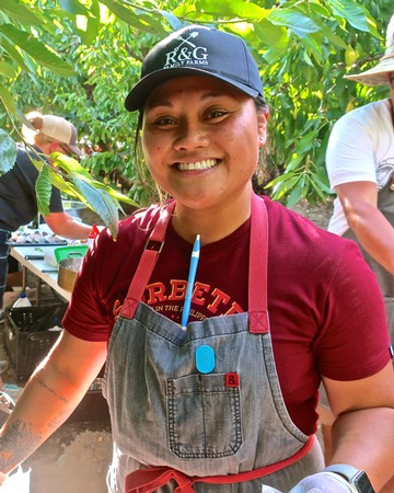 Smiling woman in vineyard wearing cap and apron at Lodi Winegrape Commission event.