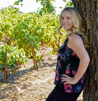 Smiling woman leaning against a tree in a vineyard during sunny day in Lodi Wine Region.