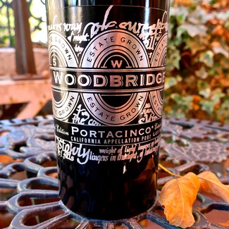 Close-up of a Woodbridge wine bottle with Lodi Winegrape Commission label, autumn leaves, and outdoor setting.