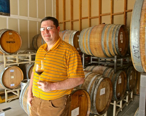 Man tasting wine in a winery with wine barrels in the background, representing Lodi wine industry.