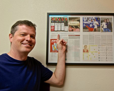 Man pointing at framed newspaper articles and images related to Lodi Winegrape Commission.