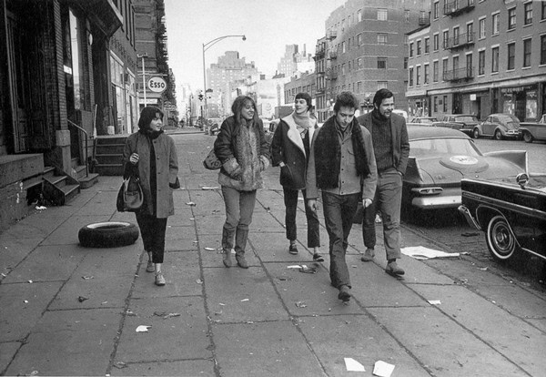 Young adults walking together on a city sidewalk, urban street scene with buildings and cars in the background.