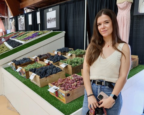 Young woman at a wine grape display booth with various grape varieties in boxes.