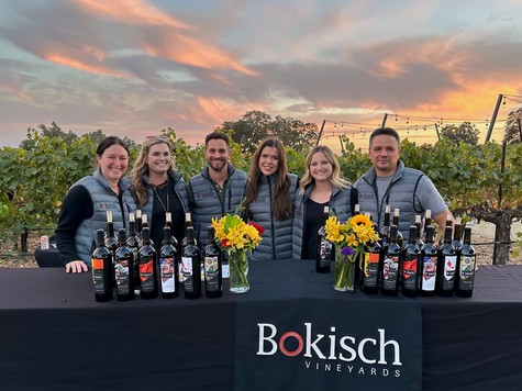 Group of people at Bokisch Vineyards with wine bottles and sunset in the background.