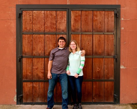 Two people standing in front of a large wooden door at a Lodi Winegrape Commission event.