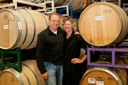 Smiling couple at winery with large wine barrels in Lodi, California.