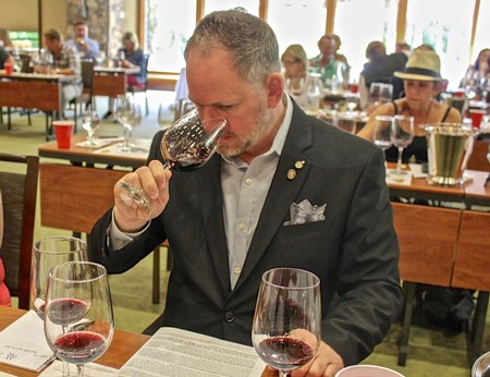 Man smelling red wine at a wine tasting event with other attendees in the background.