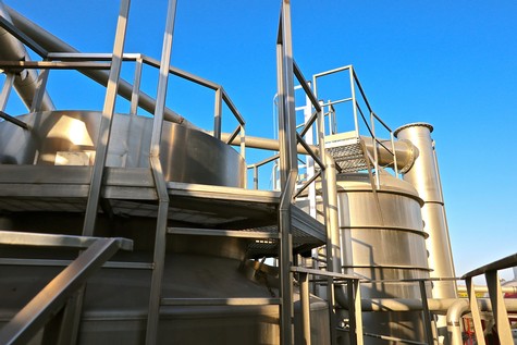Industrial wine production tanks at the Lodi Winegrape Commission facility under a clear blue sky.