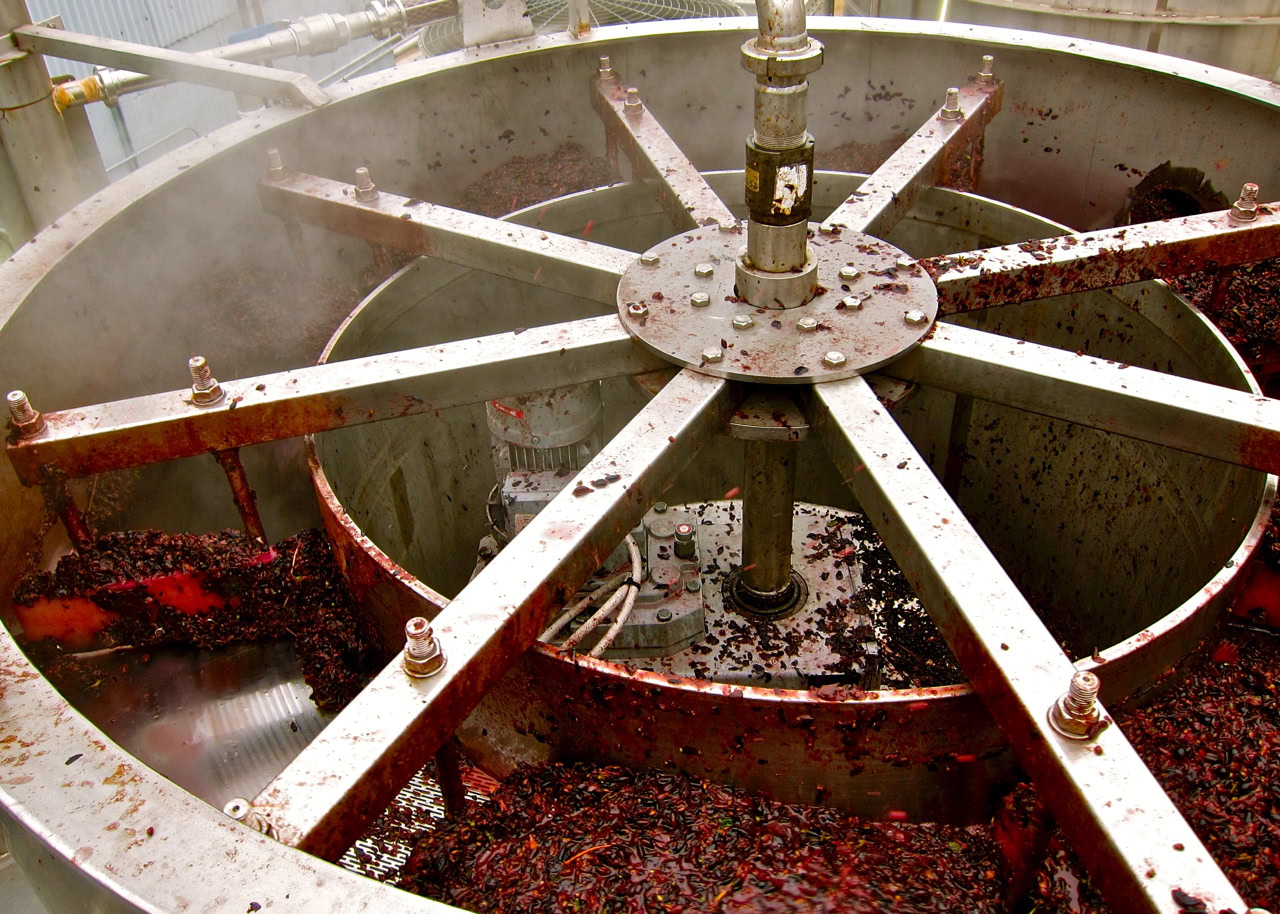 Industrial grape crushing machine used in Lodi wine production with rotating blades and stainless steel components.